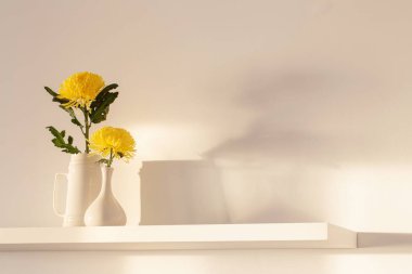 Beyaz arkaplanda beyaz rafta vazoda sarı kasımpatı