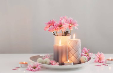 Beyaz iç kısımda yanan mumlar ve pembe ve beyaz kasımpatılar.