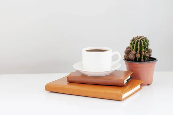 cup of coffee with notebook and cactus on white table