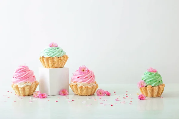 Rosa Und Grüne Cupcakes Mit Frühlingsblumen Auf Holzpodesten Auf Weißem — Stockfoto