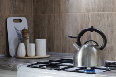 Gaz ocağında metal gümüş çaydanlık ve mutfakta mutfak gereçleri.