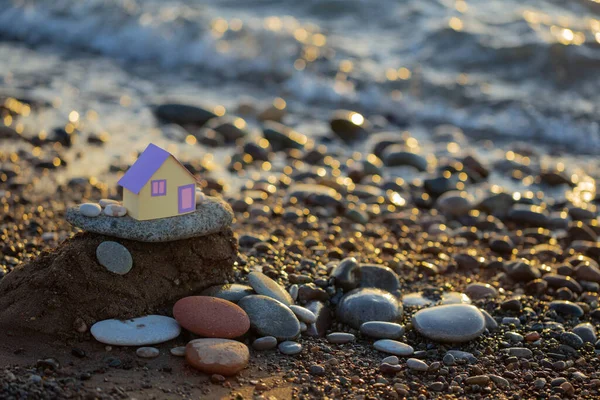 日没時の海を背景にした小さな紙の家不動産サービスの概念これらによる家の夢 — ストック写真