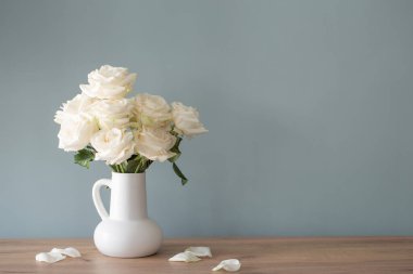 Arka planda mavi duvarda sürahide beyaz güller.