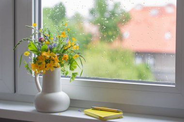Pencere kenarında beyaz sürahi içinde yaz çiçekleri