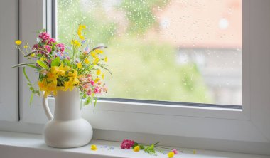 Pencere kenarında beyaz sürahi içinde yaz çiçekleri