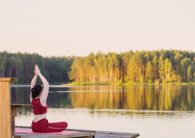Yazın göl kenarındaki ahşap iskelede yoga yapan kız.