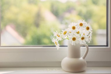Pencere pervazında beyaz sürahi içinde papatya çiçekleri