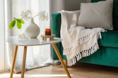 Vazoda beyaz rhododendron dalı ve modern rahat iç mekanda yanan mumlar.
