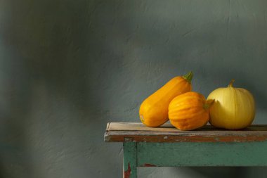 Arkadaki yeşil duvarda eski ahşap masada turuncu balkabakları