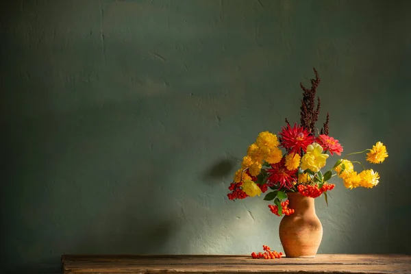 红色和黄色的花朵挂在水壶上 阳光照射在黑暗的墙壁上 — 图库照片
