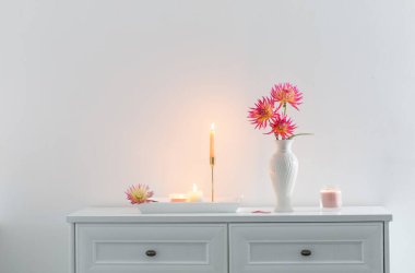 Beyaz vazoda güzel pembe yıldız çiçekleri ve beyaz arka planda yanan mumlar.