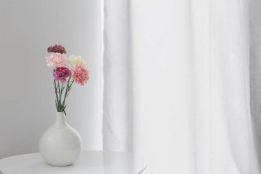 Beyaz masadaki seramik vazoda karanfil çiçekleri