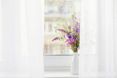 Beyaz pencere eşiğindeki yaz buketi yağmur damlaları