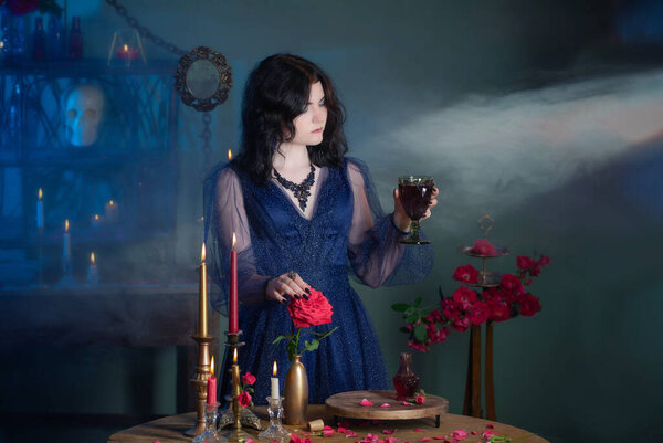 Young beautiful woman in blue vintage dress with red roses makind potion in dark room