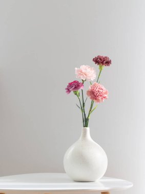 Beyaz masadaki seramik vazoda karanfil çiçekleri