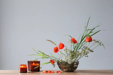 Vahşi çiçeklerin ve bitkilerin gri arka planda cam kasede sıralanması