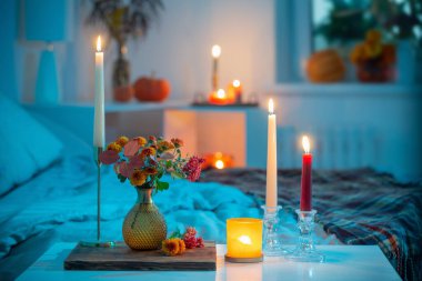 Vazoda sonbahar kasımpatısı ve yatak odasında yanan mumlar.