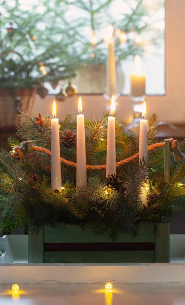 在家里的白色桌子上用冷杉树枝和四个燃烧的蜡烛装饰木制篮子 — 图库照片