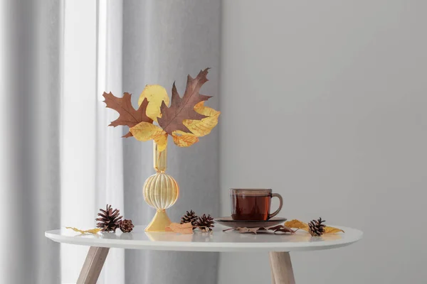 背景灰墙玻璃花瓶里的一杯茶和秋天的叶子 — 图库照片