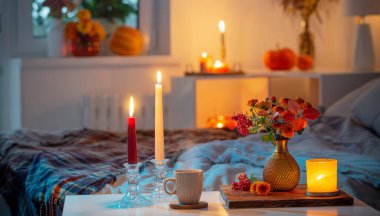 Bir fincan çay ve vazoda kasımpatı ve yatak odasında yanan mumlar.