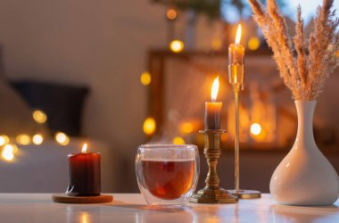 Termo bardakta sıcak çay, yılbaşı süsü ve evde yanan mumlar.