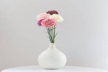 Beyaz masadaki seramik vazoda karanfil çiçekleri