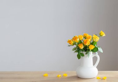 Tahta rafta beyaz sürahide sarı güller