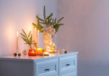 Beyaz odada yanan mumlarla Noel süsleri.