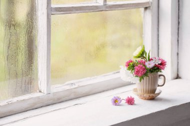Çiçekler küçük bardakta eski beyaz pencere pervazında