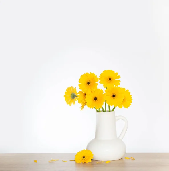 stock image yellow gerbera in  white jug  on wooden shelf  on background wall