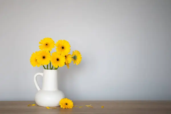 stock image yellow gerbera in  white jug  on wooden shelf  on background wall