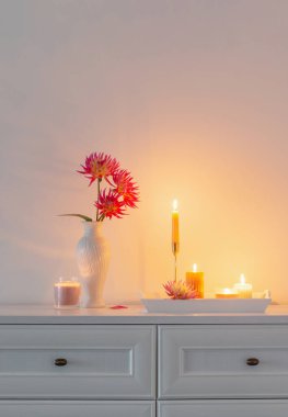 Beyaz vazoda güzel pembe yıldız çiçekleri ve beyaz arka planda yanan mumlar.