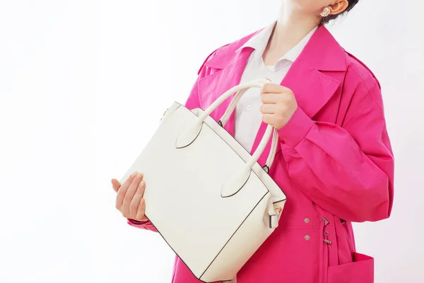 woman in pink trench coat with white handbag