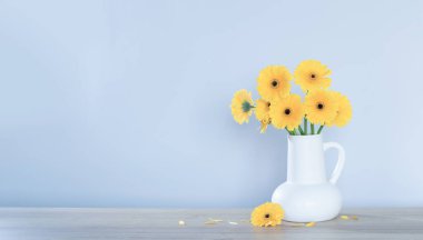 Beyaz sürahi içinde sarı gerbera arka plandaki ahşap rafta.