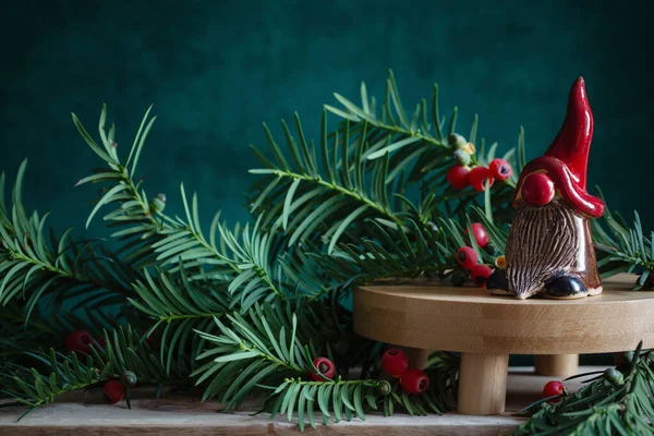 濃い緑の背景にクリスマスの枝が付いている赤い帽子の陶磁器のノーム — ストック写真