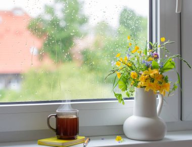 Beyaz sürahide yaz çiçekleri Pencere kenarında bir fincan çayla