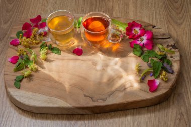 Cam fincanlarda bitki çayı, çiçekler ve ahşap arka planda bitkiler.