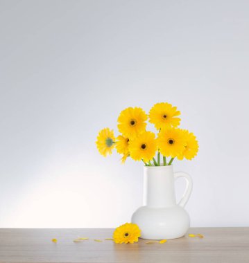 Beyaz sürahi içinde sarı gerbera arka plandaki ahşap rafta.