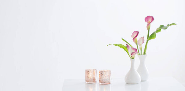 pink calla lily in vase  and burning candles on white background