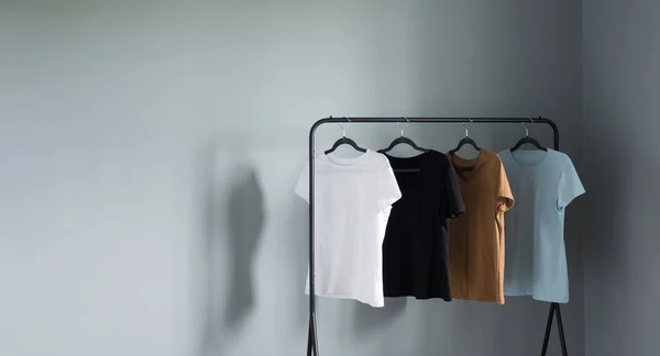 灰色の壁に対する黒のハンガーに中立色のTシャツ — ストック写真