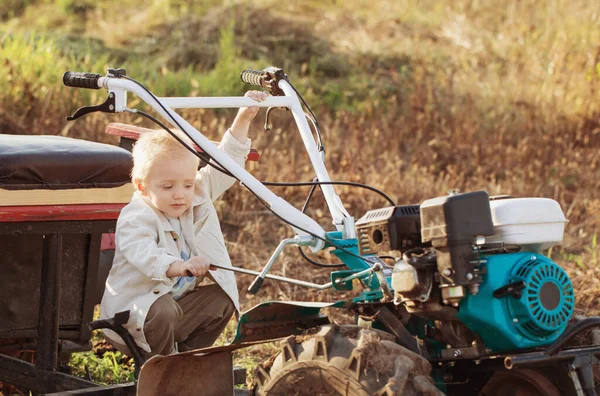 一个滑稽的小男孩坐在田里的后排拖拉机上 — 图库照片