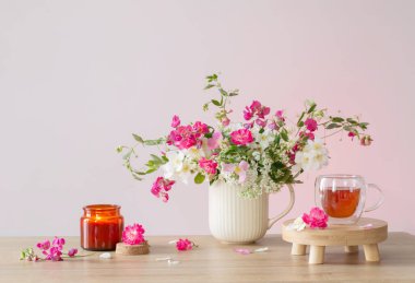 Yaz çiçekleri, yanan mumlar ve arka planda bir fincan çay.
