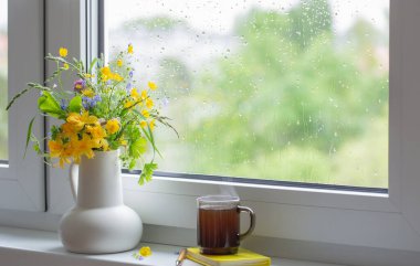 Beyaz sürahide yaz çiçekleri Pencere kenarında bir fincan çayla