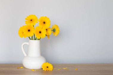 Beyaz sürahi içinde sarı gerbera arka plandaki ahşap rafta.