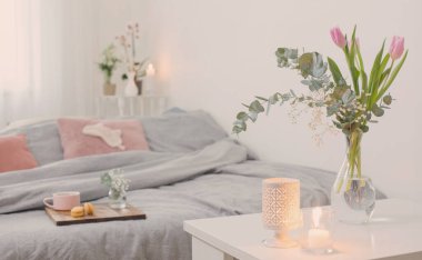 Yatak odasının içinde çiçekler, mumlar ve bir fincan çay var.