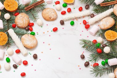 Beyaz mermer arka planda noel ağacı dalları olan şekerler ve kurabiyeler