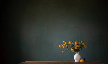 Beyaz vazoda sarı kasımpatılar. Arka plandaki siyah duvarda.