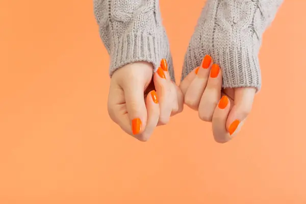female hands with orange manicure   on  orange background