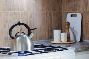 Gaz ocağında metal gümüş çaydanlık ve mutfakta mutfak gereçleri.