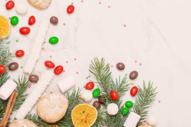Beyaz mermer arka planda noel ağacı dalları olan şekerler ve kurabiyeler
